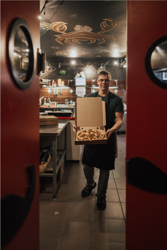 pizzeria employee holding a pizza in the kitchen